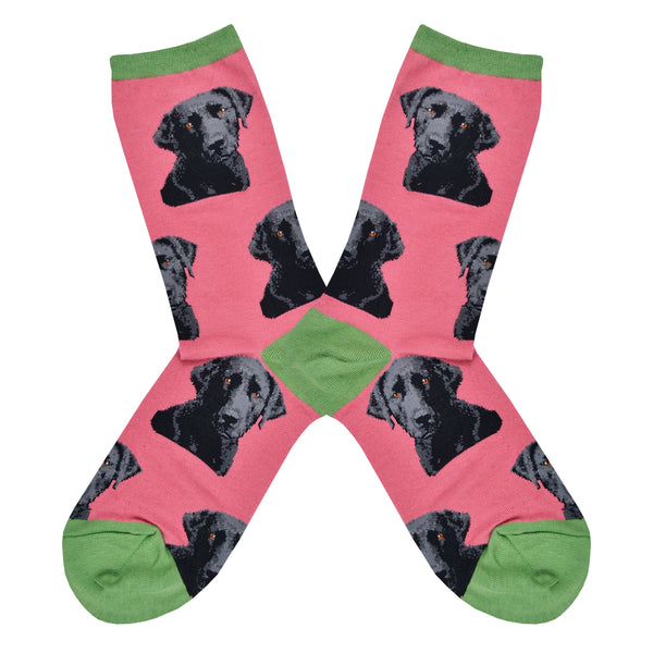 Shown in a flat lay, a pair of women's fit Sock Smith cotton crew socks in pink with a green heel, toe, and cuff. These socks have realistic black labs all over the sock. 