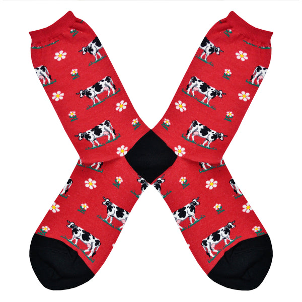 Shown in a flatlay, a pair of women red crew socks with a black heel and toe. The socks feature an all over design off black and white cows and little daisy's. 