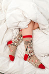 "I Hate Eveyone, Too" socks shown on a model's feet in a cozy bed with messy sheets as the background.