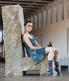 A short haired model in a blue floral dress sits on a cement chair while wearing the "I'm a delicate fucking flower" socks