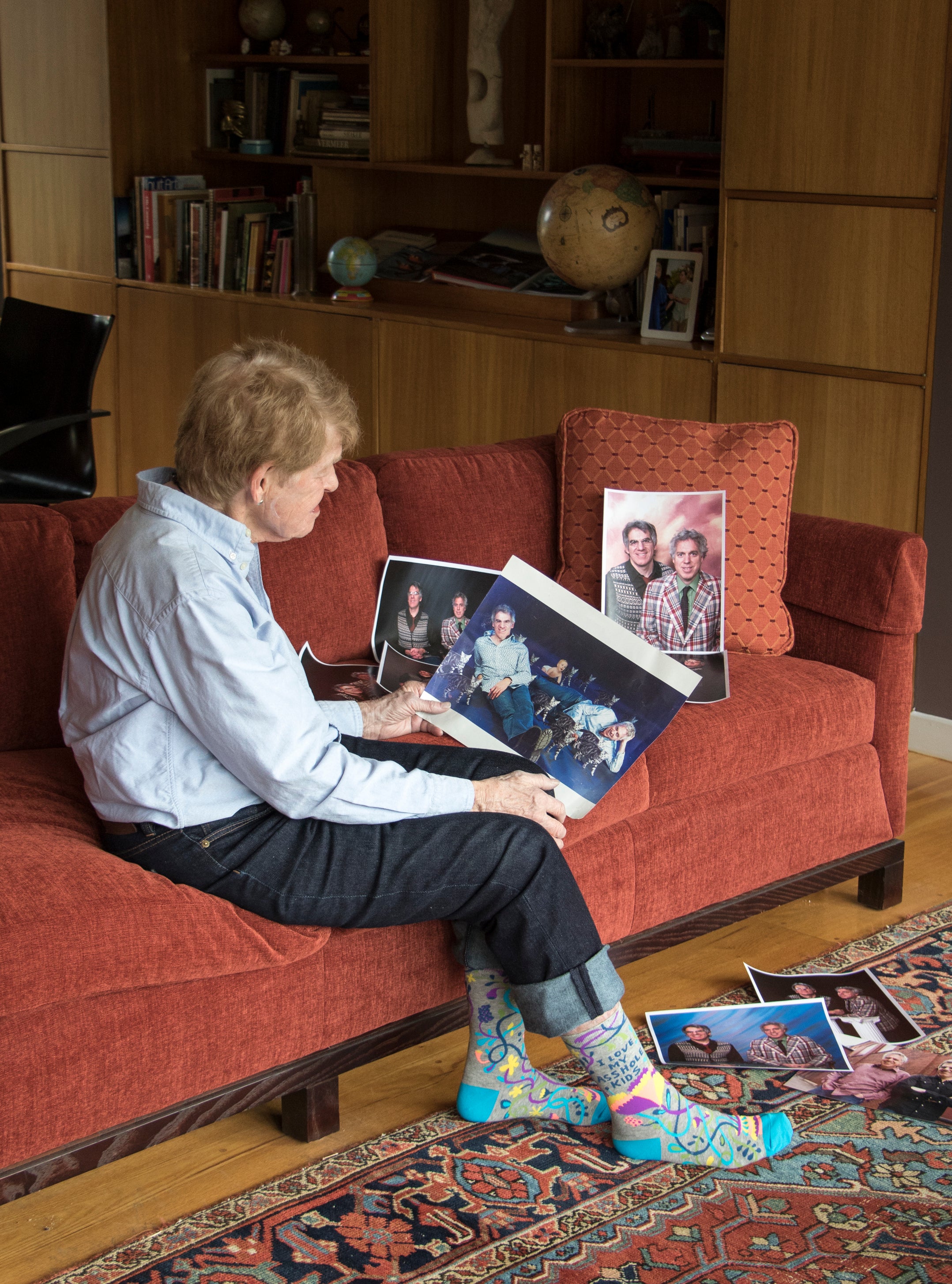 An older man is pictured sitting on a red couch looking at old photos of his family. On his feet are the 