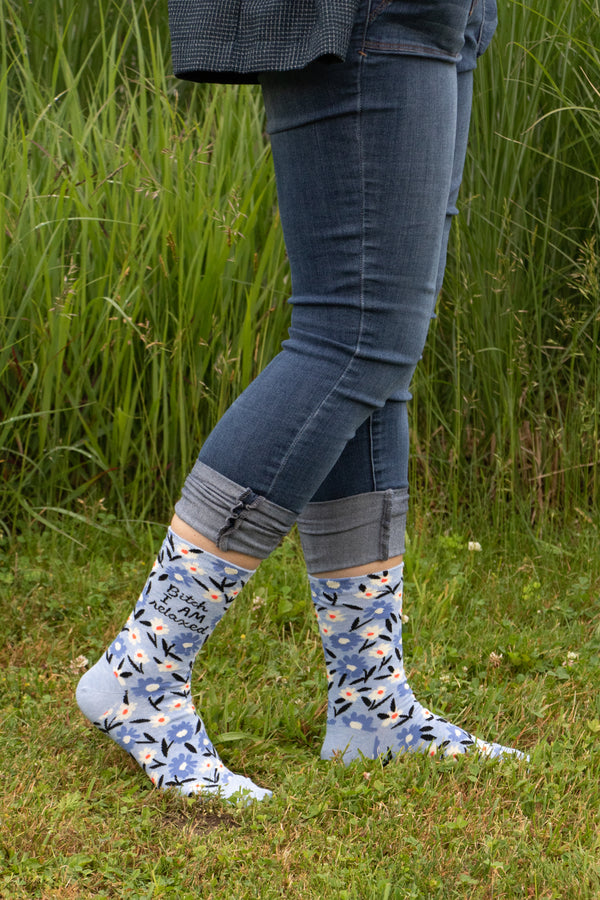 "Bitch I am Relaxed" blue floral socks shown on a models feet. They are pictured walking in a grassy field. 