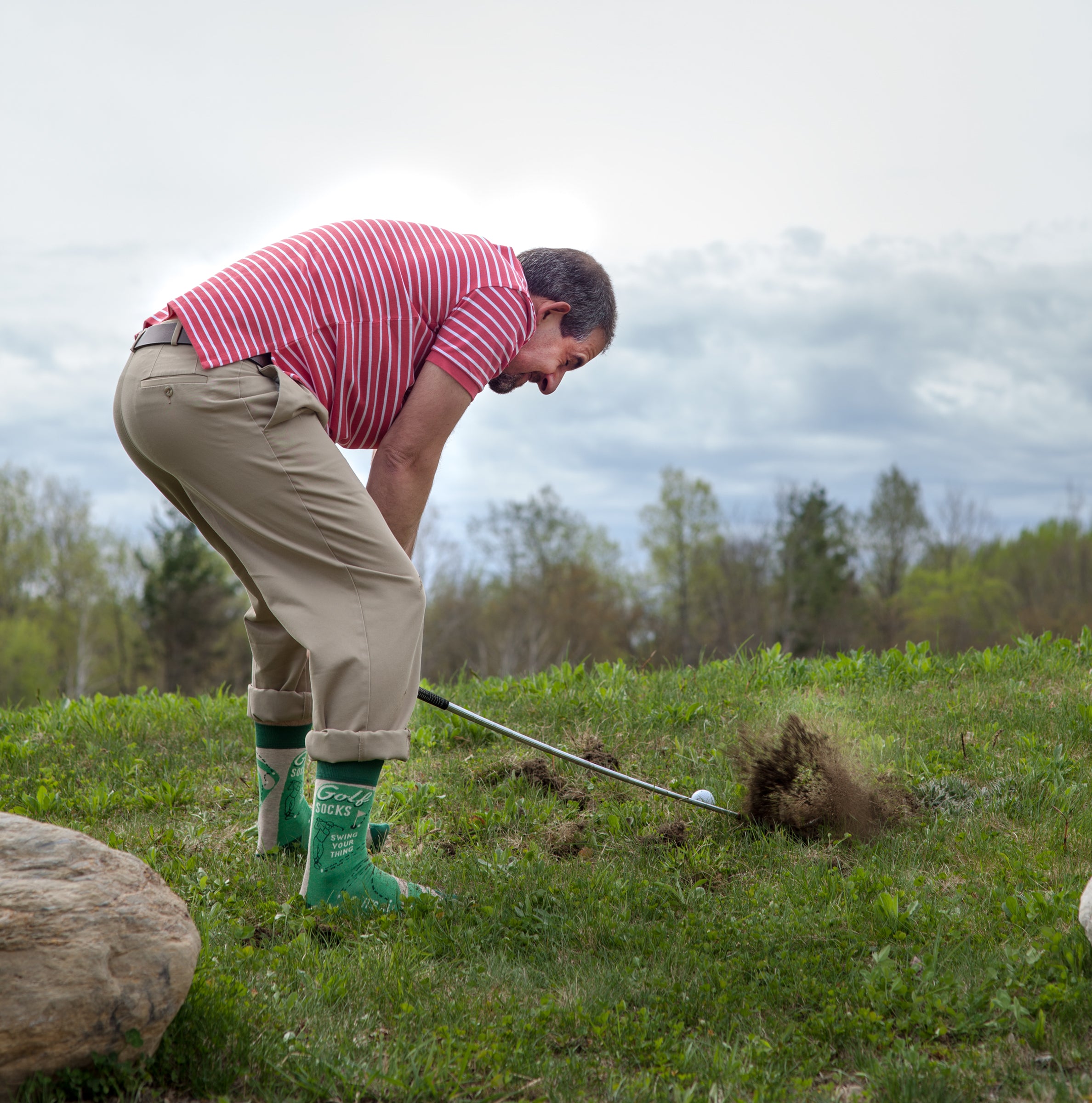 Photo of a man crouched down to make a difficult golf shot. He is wearing the advertised Blue Q golf socks.