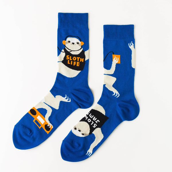 Shown in a relaxed flatlay, a pair of Yellow Owl Workshop’s royal blue nylon-cotton men's crew socks with large sloths listening to music, holding boomboxes and wearing shirts that say “Sloth Life,” “Naps,” “Slow Jams” or “Weekends”