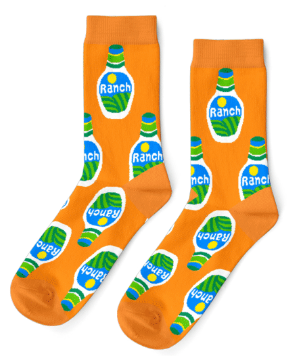 Shown in a flatlay, a pair of men's orange socks with bottles of ranch dressing all over. Hidden Valley of course!