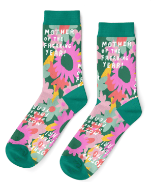 A pair of teal socks lie on a white background. They feature mint green, orange, pink, yellow and peach daisies drawn in spatter style and white text that reads "Mother of the Freaking Year!"