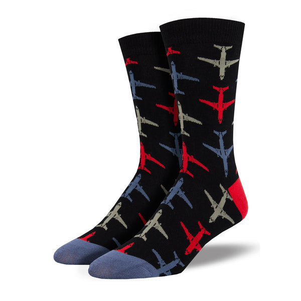 Shown on leg forms, a pair of men's Socksmith brand bamboo black socks with a red heel and blue toe. These socks have an all over motif of red, grey, and blue airplanes going up and down the sock.