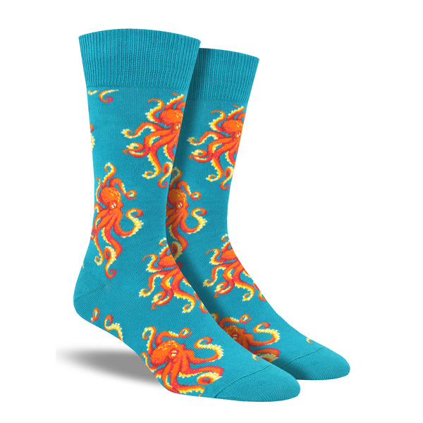 Shown on a leg form, these colorful teal cotton men's crew socks by the brand Socksmith feature bright orange Octopus in a repeated pattern on the foot and leg.