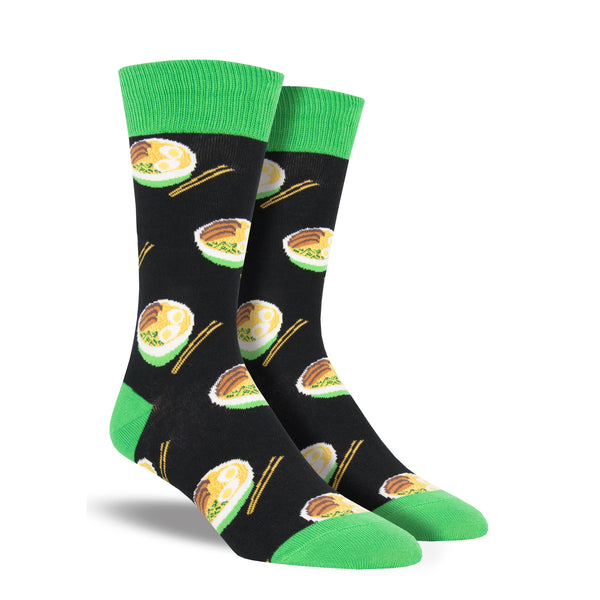 Shown on leg forms, a pair of Socksmith brand men's cotton crew socks in black with a green cuff/heel/toe featuring  an all over motif of bowls of ramen and chopsticks.