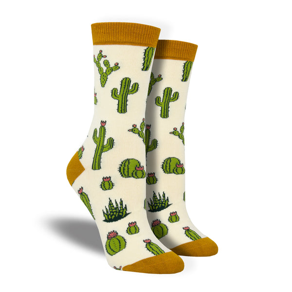 Shown on leg forms, a pair of Socksmith brand women's bamboo crew socks in cream with a gold toe, heel, and cuff. This sock features different types of cactus plants in shades of green all over the sock.