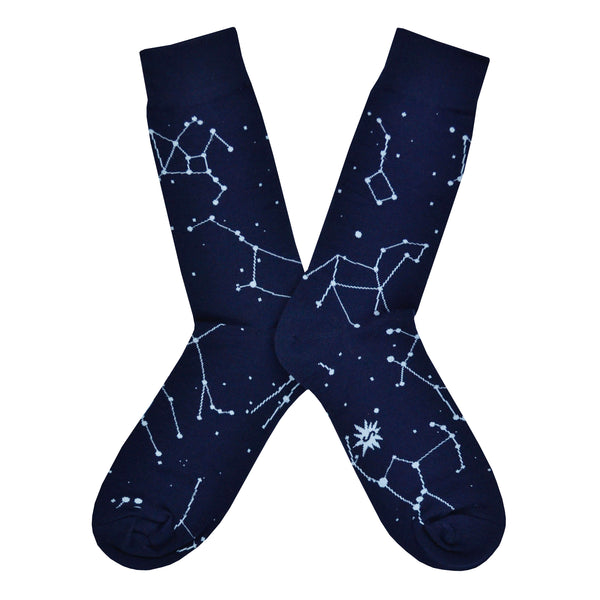 Shown in a flatlay, a pair of Sock It To Me navy blue cotton men's crew socks with glow in the dark constellation all over pattern
