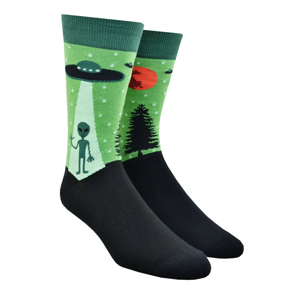Shown on a foot form, a pair of Sock It To Me green cotton men's crew socks with alien waving goodbye as it gets sucked into a UFO