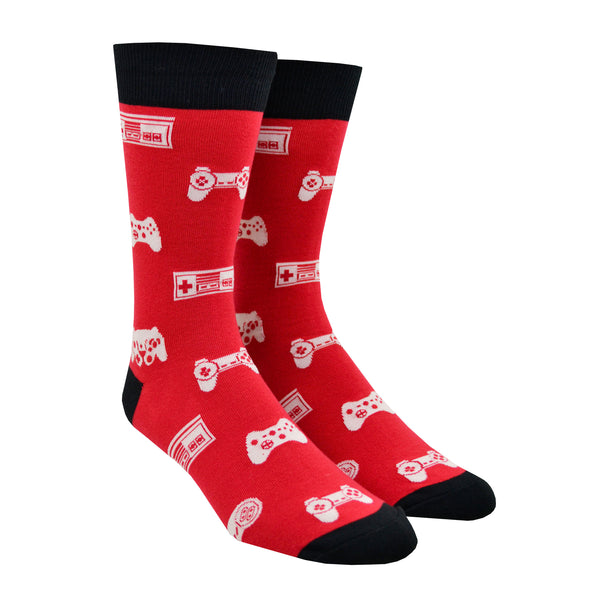 Shown on leg forms, a pair of Sock it to Me brand men's cotton crew socks in red with a black heel, toe, and cuff. These socks feature various vintage game controllers in white all over the sock.