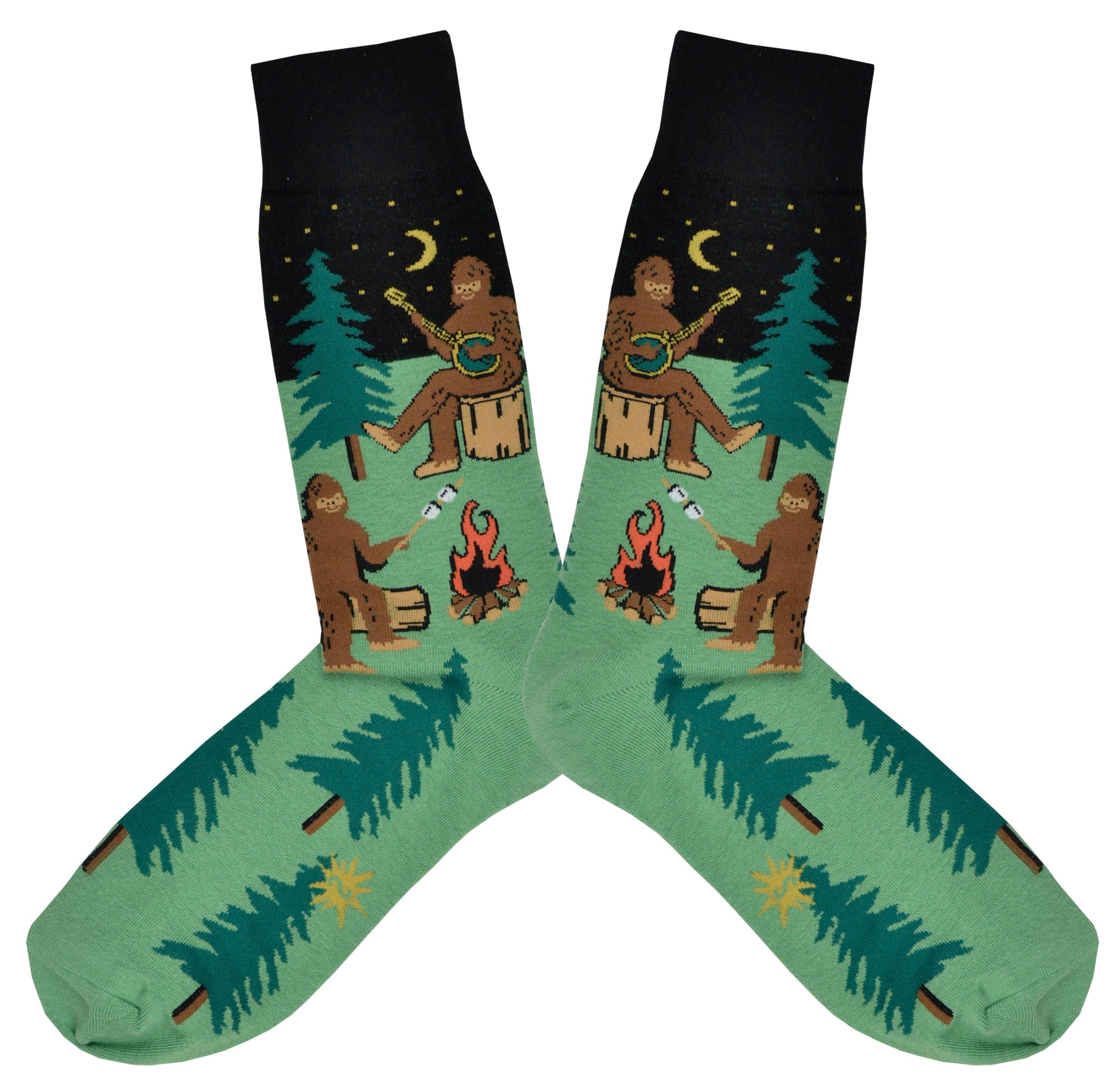 Shown in a flatlay, a pair of Sock It To Me green cotton men's crew socks with black starry sky and various sasquatches enjoying a campfire (playing banjo, roasting marshmallows) among a pine forest