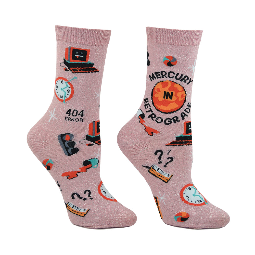 Shown on a leg form, these pink glittery women's crew socks by the brand Sock it To Me feature the words Mercury in Retrograde on the leg with small images of things going wrong throughout, like spilt coffee, a computer crashing and red stop lights.
