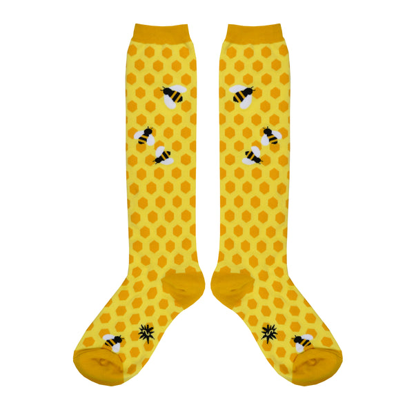 Shown in a flatlay, a pair of Sock It To Me cotton knee high extra-stretchy socks in yellow with honeycomb pattern and some bees near the knees