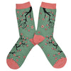 Shown in a flatlay, a pair of Socksmith brand women's bamboo crew socks in sage green with a pink heel, toe, and cuff. This sock features an all over design cherry blossom branches reaching around the sock.