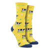 Shown on leg forms, a pair of women's crew socks in yellow with a navy blue heel and toe. These socks have an all over design of black and white cows and daisy's.