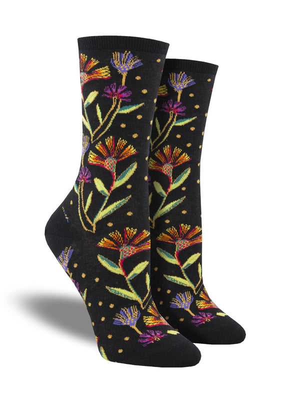 Shown on a leg form, these black cotton women's crew socks by Socksmith feature the artwork of Laurel Burch and have colorful flowers woven with metallic threads all over the leg and foot.