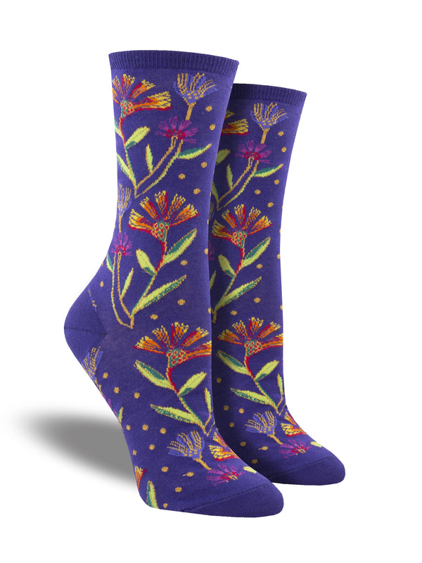 Shown on a leg form, these purple cotton women's crew socks by Socksmith feature the artwork of Laurel Burch and have colorful flowers woven with metallic threads all over the leg and foot.