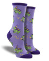 Shown on a leg form, these purple cotton women's crew socks with a dark purple heel, toe and cuff by the brand Socksmith feature cute green frogs wearing purple wizard outfits and hats, holding a wand with stars coming out of it.