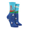 Shown on a leg form, these blue cotton women's crew socks by the brand Socksmtih feature the iconic landmark of San Francisco, the Golden Gate Bridge, on a clear sunny day towering above the beautiful bay filled with sailboats.