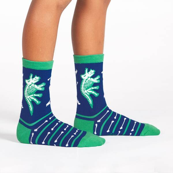 a child's legs wearing a pair of blue socks with green stripes and white dinosaur skeletons on a white background