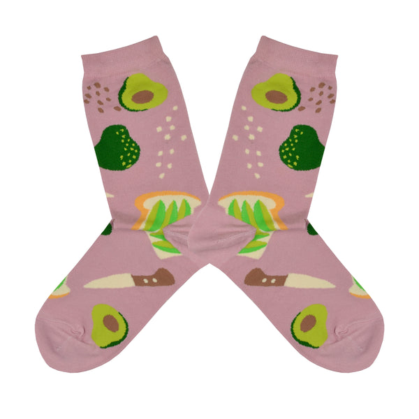Shown in a flatlay, a pair of Yellow Owl Workshop brand women's cotton crew socks in a light brown with an avocado toast theme. Each sock features avocado toast, avocados, salt and pepper, and a knife.