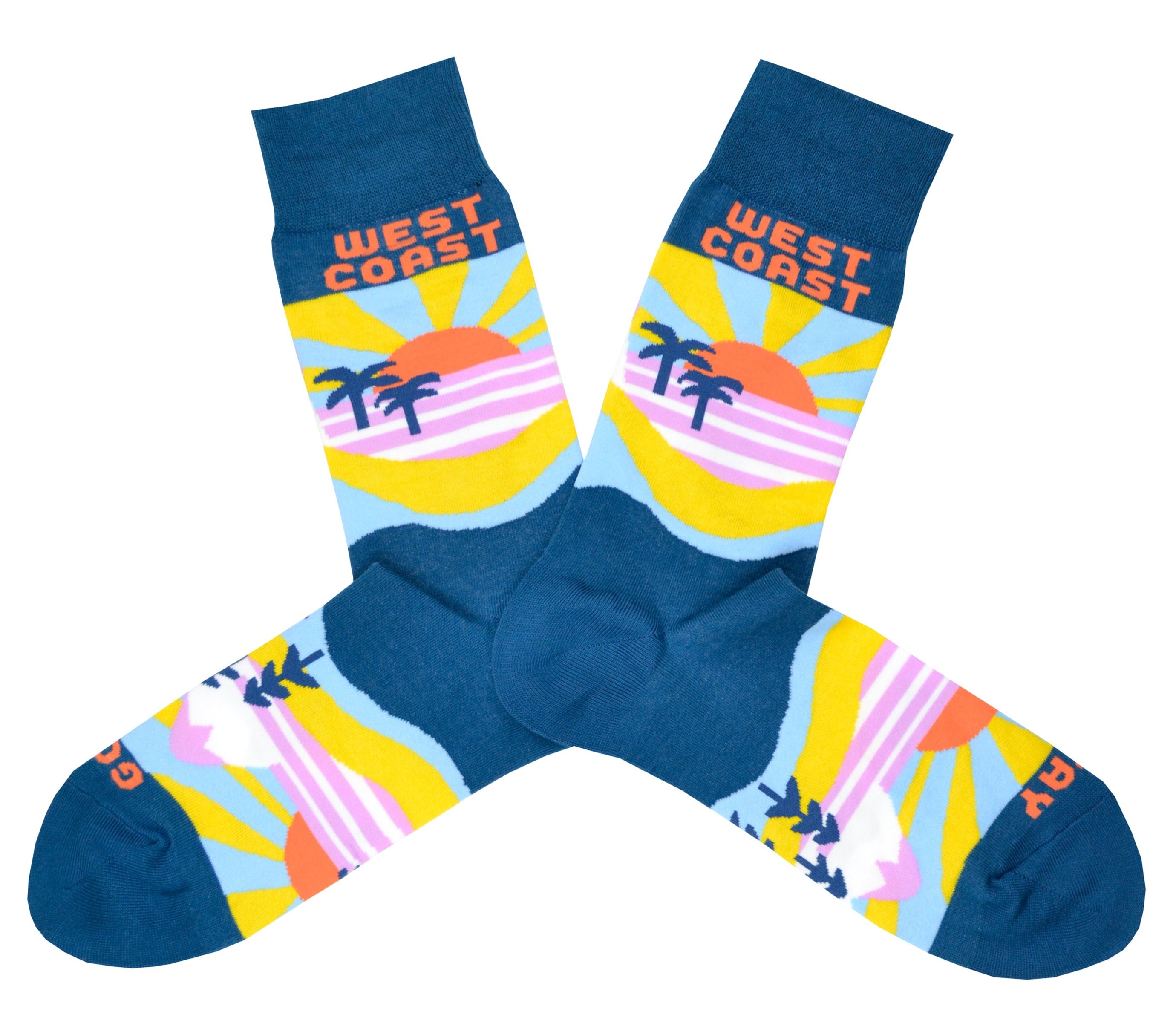 These blue cotton men's novelty crew socks by the brand Yellow Owl Workshop feature an orange and yellow sun setting over a pink landscape with blue palm trees and say the words 