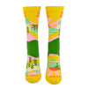 A front view on a leg form, these yellow cotton women's novelty crew socks by the brand Yellow Owl Workshop feature green trees, teal and white mountains, and pink clouds and say the words "West Coast Best Coast" near the cuff and "Stay Gold" by the toes.