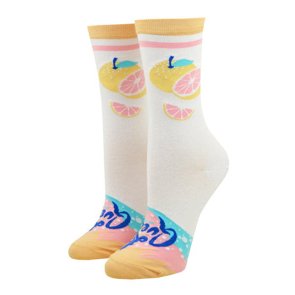 Shown on a leg form, these white cotton cute women's crew socks with a peach toe and cuff by the brand Yellow Owl Workshop feature a can that says "La Queen" on one side, and two grapefruit, one sliced and one whole, on the other side, and near the toe there's peach, pink and light blue swirls that resemble the design of the La Croix can, bubbles and the words "La Queen".