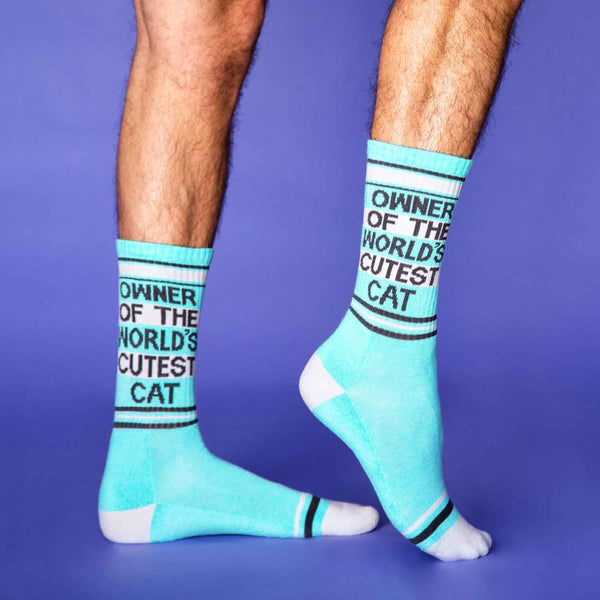Model's feet wear blue crew socks with gray & black stripe patterns & text that reads "OWNER OF THE WORLD'S CUTEST CAT"