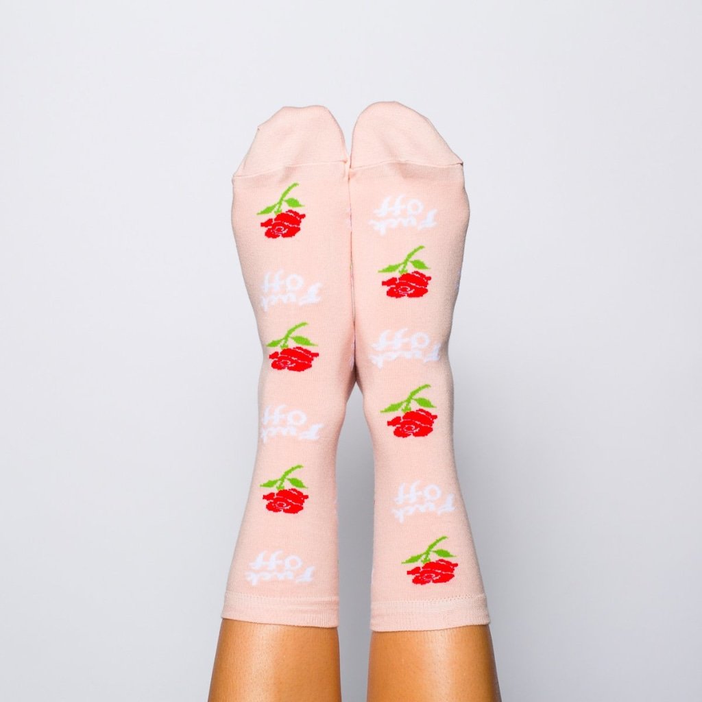 Shown on a models feet from the front, a pair of women's Yellow Owl Workshop pink cotton crew socks with an all over rose and 