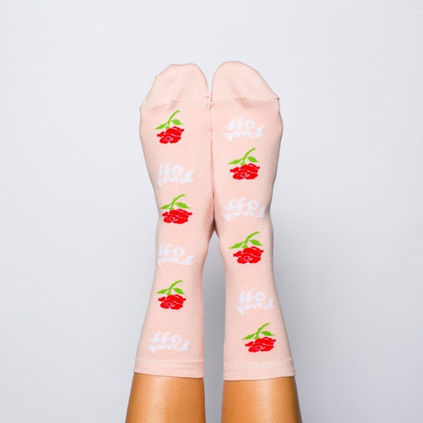 Shown on a models feet from the front, a pair of women's Yellow Owl Workshop pink cotton crew socks with an all over rose and "Fuck Off" motif in white font.