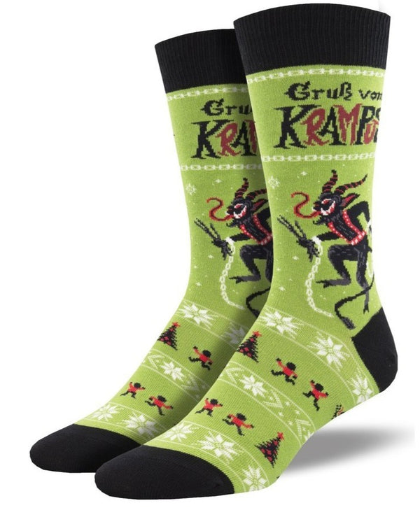  Shown on a leg form, these green cotton men's crew socks with a black heel, toe and cuff by the brand Socksmith show the German Folklore character of Krampus coming to terrorize misbehaving children on Christmas Eve.