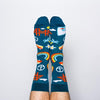 Model wearing a pair of Yellow Owl Workshop’s navy blue nylon-cotton men's crew socks with San Francisco Golden Gate Bridge, peace sign, palm tree, daisy, VW bus and highway One sign