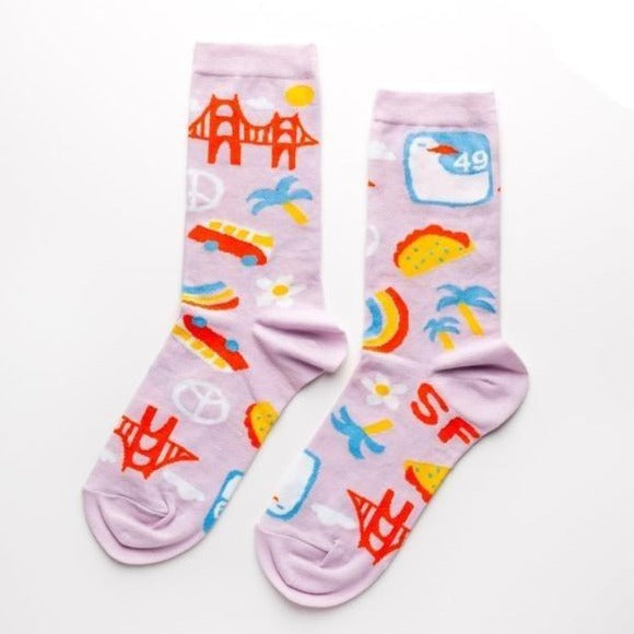 Shown in a flatlay, a pair of women's Yellow Owl Workshop cotton and nylon crew socks in lilac. These socks feature iconic San Francisco imagery like the golden gate bridge, peace signs, VW vans, seagull signage, and flower power.