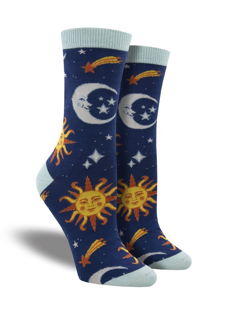 Shown on a leg form, these dark blue bamboo womens crew socks with a light blue heel, toe and cuff by the brand Socksmith feature a smiling yellow and orange sun, smiling gray moon  and orange shooting stars.