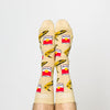 Model wearing a pair of Yellow Owl Workshop’s tan nylon-cotton men's crew socks with browning bananas and red soup cans